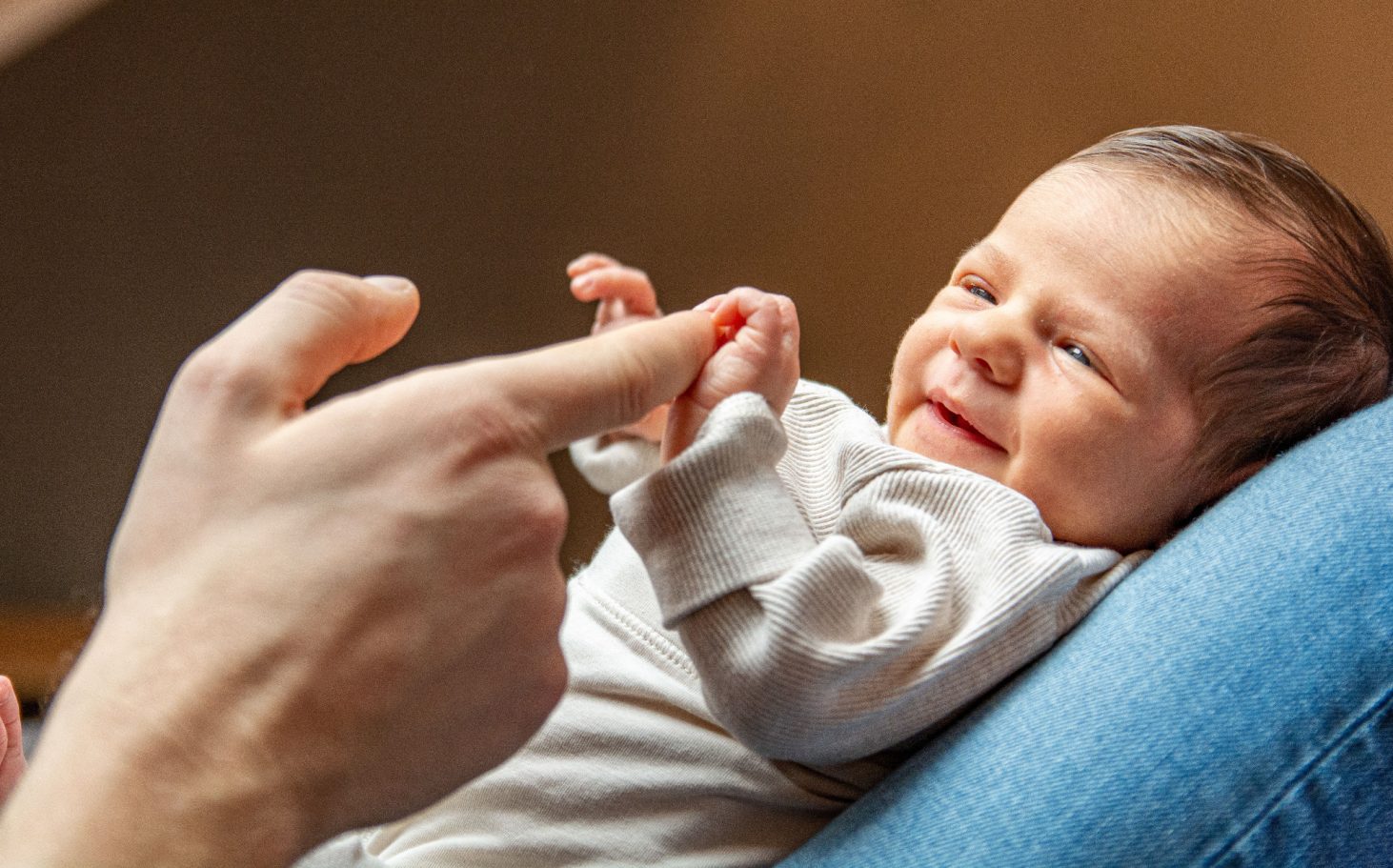 NEWBORN Ein Lächeln eines Babys, das mit einer Hand spielt und Freude ausstrahlt.