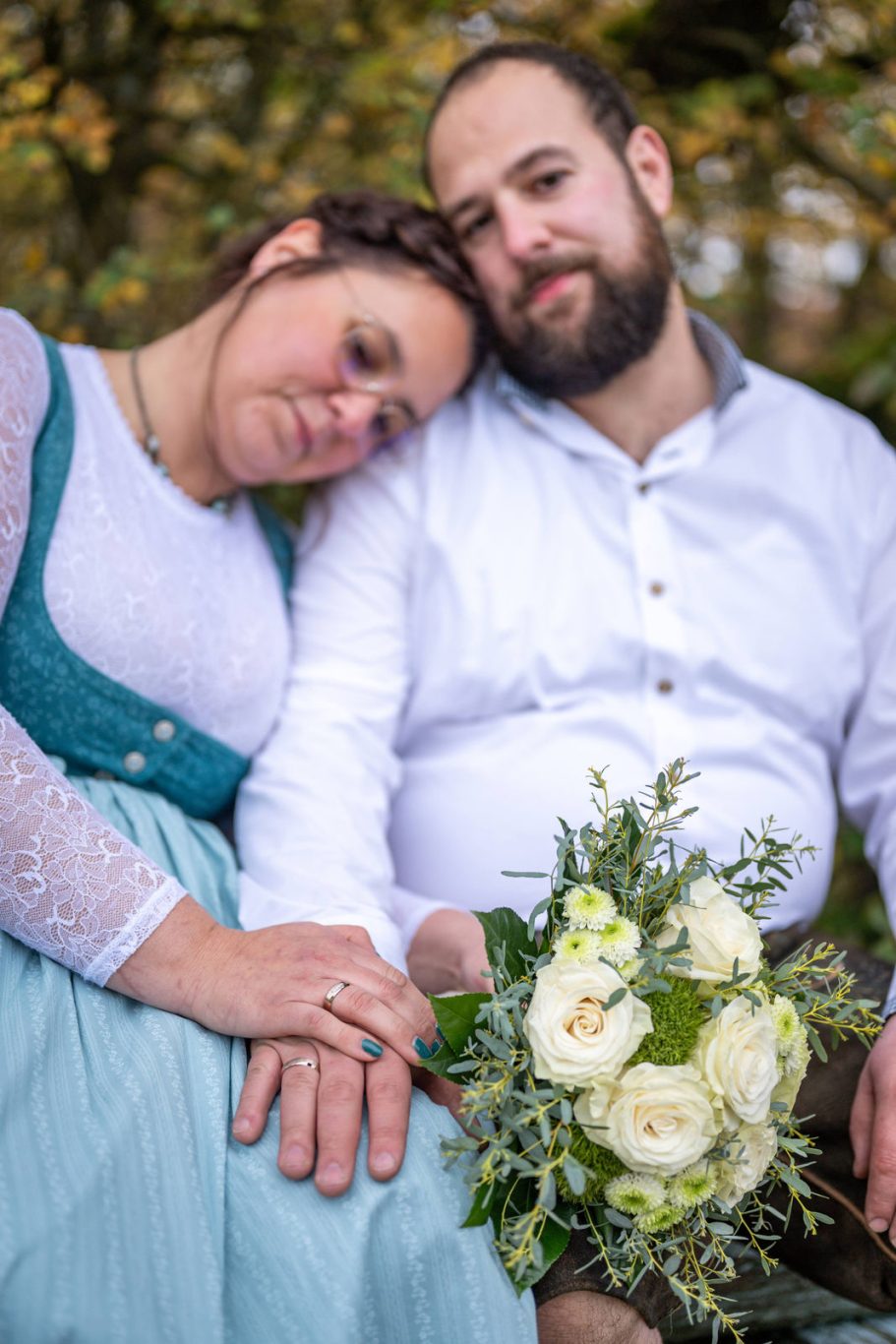 Paar sitzt zusammen im Freien, umarmt sich, mit einem Brautstrauß aus weißen Rosen.