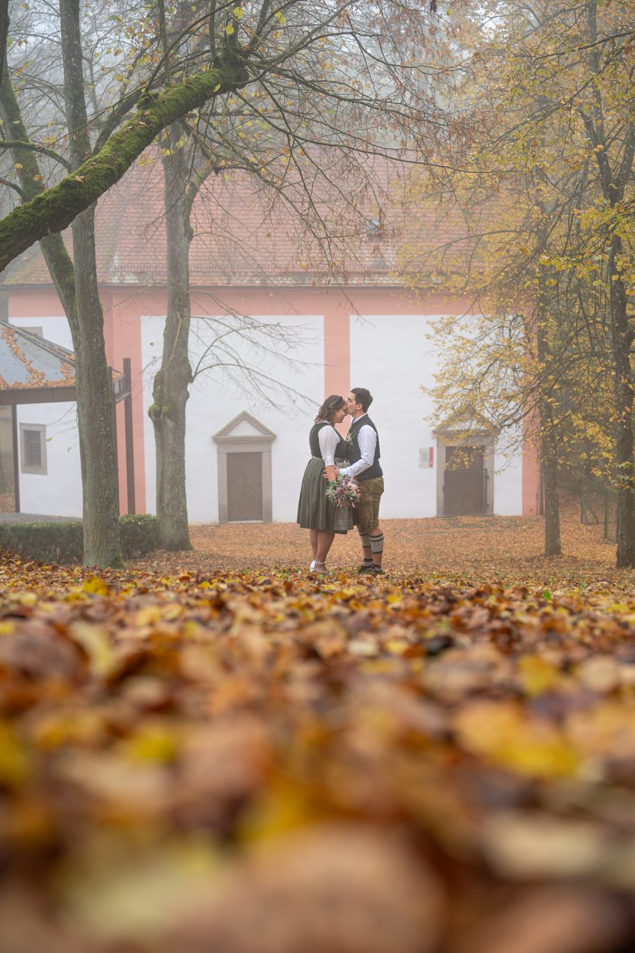 Paar umarmt sich in einem herbstlichen Park mit buntem Laub und nebliger Kulisse.