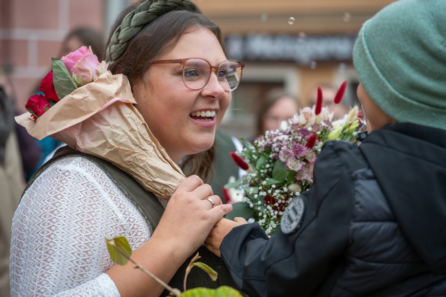 Frau mit Blumenstrauß lächelt, während ein Kind ihr Blumen überreicht.