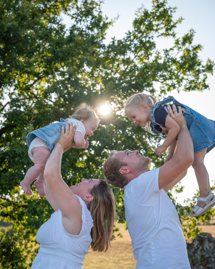 Familie mit zwei kleinen Kindern, die im Freien miteinander spielen und lachen.