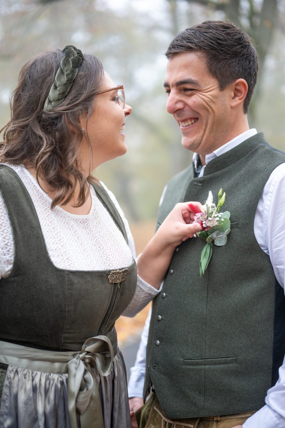 Braut und Bräutigam lachen und betrachten sich in traditioneller Tracht im Freien.