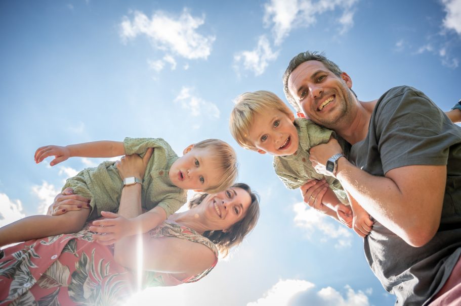 Familie mit zwei kleinen Kindern unter blauem Himmel, lachend und glücklich.