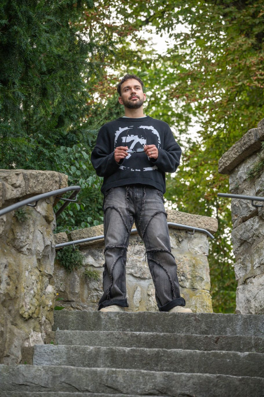 Mann steht auf einer Treppe, umgeben von Bäumen und einer Steinmauer.