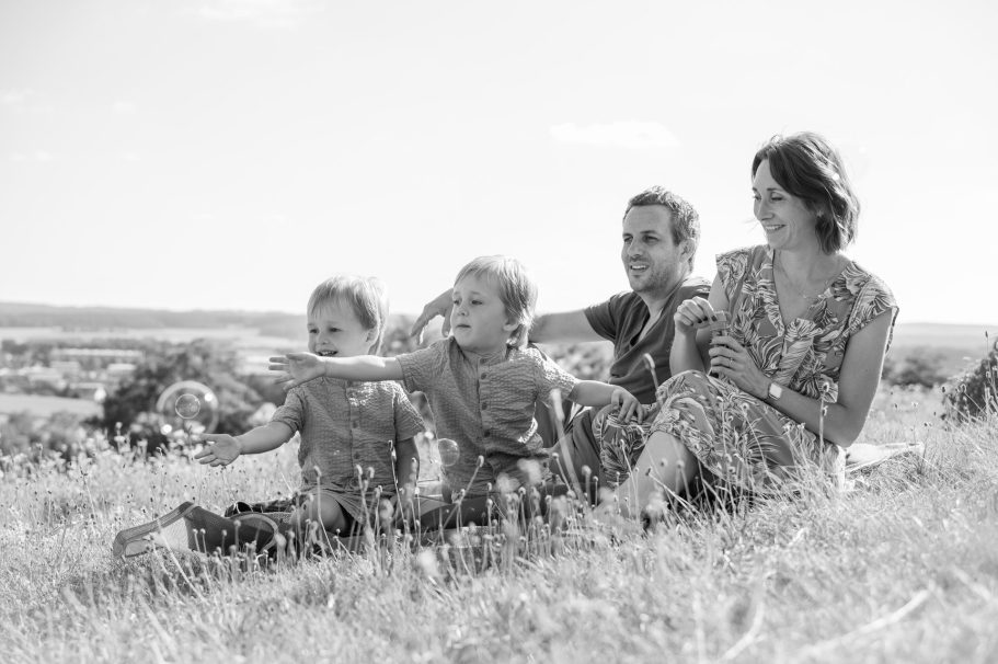 Vier Personen sitzen im Gras, zwei Kinder zeigen begeistert in die Ferne.