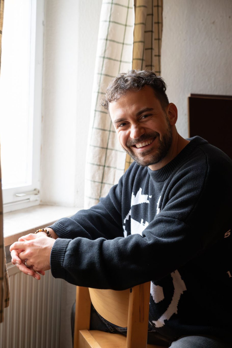 Lächelnder Mann sitzt auf einem Stuhl neben einem Fenster.