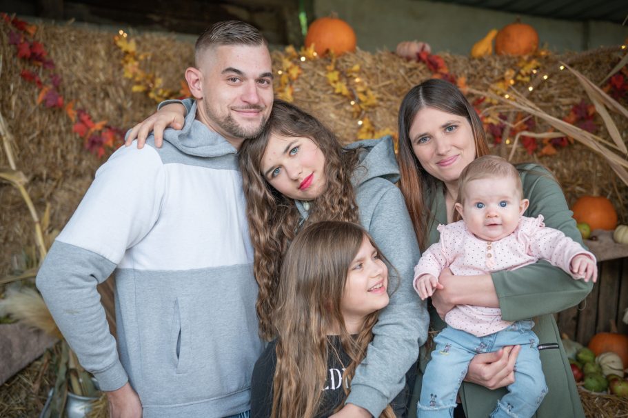 Familie posiert lächelnd vor einer herbstlichen Kulisse mit Kürbissen.