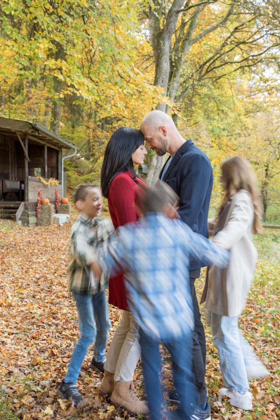 FAMILIEN Eine Familie umarmt sich in einem herbstlichen Park mit buntem Laub.