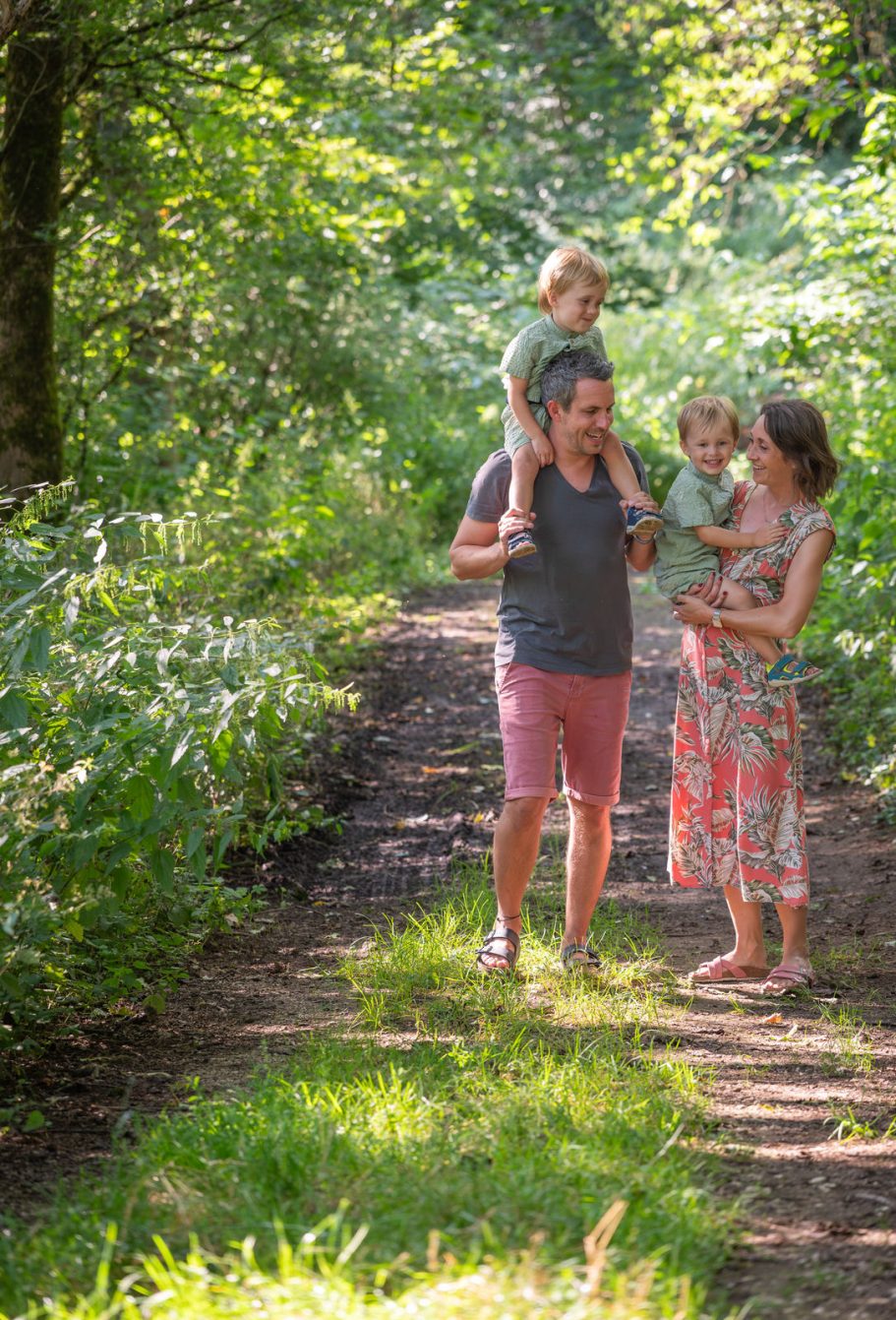 Familie mit zwei Kindern geht auf einem Waldweg im Grünen spazieren.