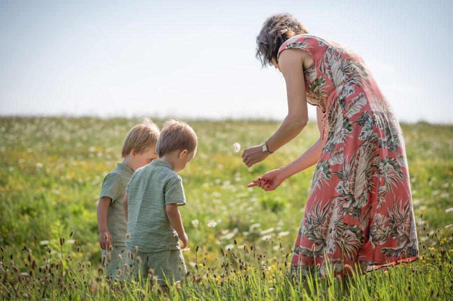 Eine Frau sammelt Blumen mit zwei kleinen Kindern in einer blühenden Wiese.