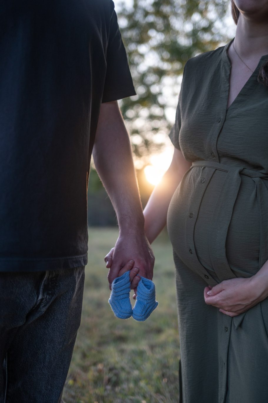 Babybauchshooting - Paar hält Babyschüchen in den Händen, Sonne im Hintergrund