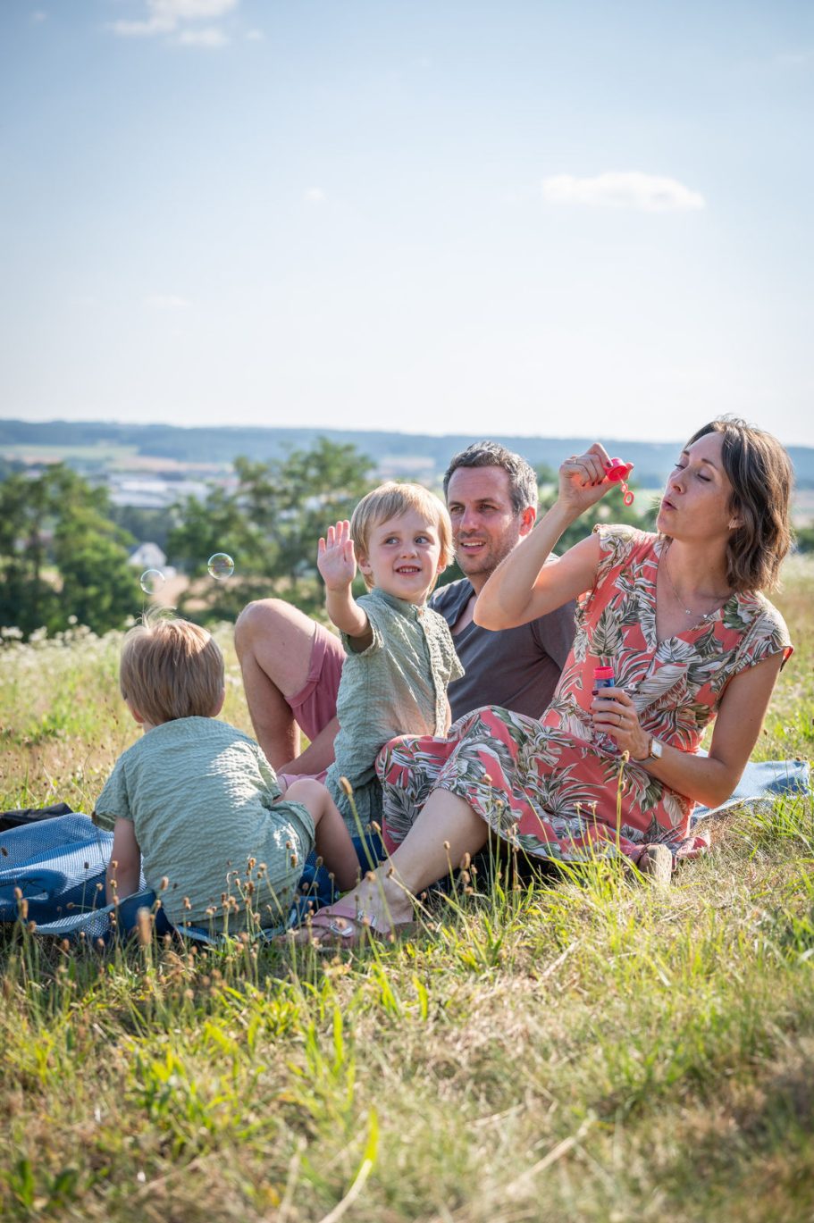 Familie sitzt auf einer Wiese, Kinder spielen mit Wasser und genießen den Sonnenschein.