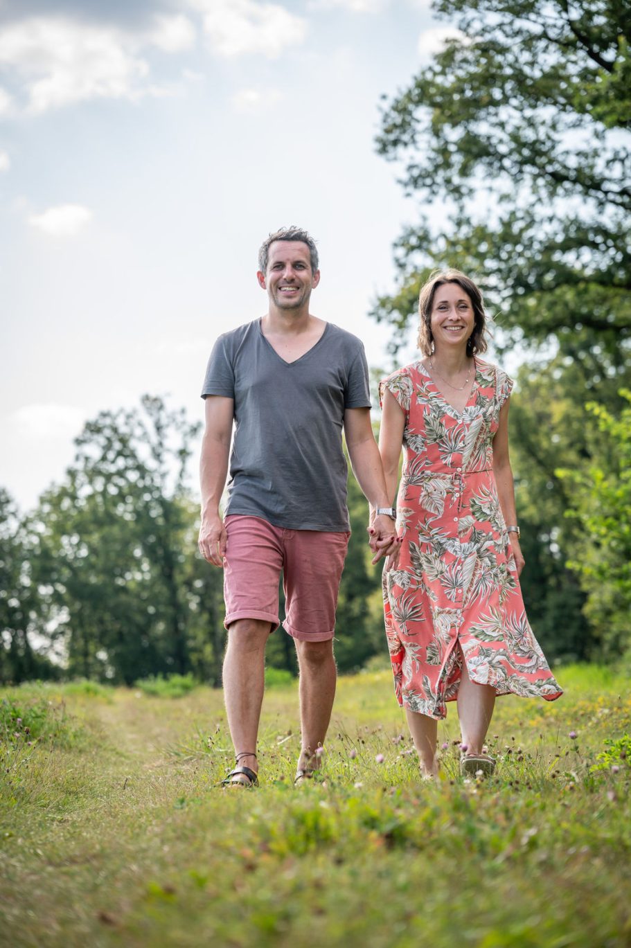 Ein Paar spaziert im Freien, Hand in Hand, umgeben von Bäumen und Gras.